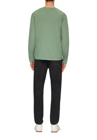 Chemise longue à manches longues vert clair avec un col rond, des manches raglan et une texture lisse, associée à un jean foncé et des baskets blanches.