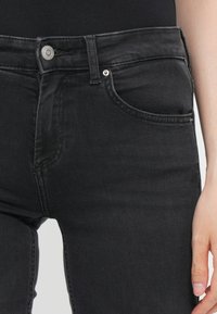 Jean en denim noir avec une coupe ajustée, doté d'une fermeture à bouton sur le devant, de deux poches latérales et d'un léger stretch pour plus de confort.