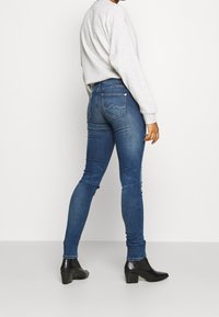 Jeans ajustados de mezclilla azul medio, de cintura alta, con un diseño de bolsillo trasero. Combinados con un sudadera gris claro y botas de tacón negras.