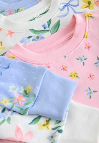 Tres sudaderas apiladas: una blanca con estampado floral, una rosa claro con pequeñas flores y una azul con un patrón de lunares.