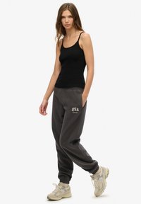 Top sin mangas negro combinado con pantalones jogger grises que presentan un logotipo bordado de "USA". El modelo lleva zapatillas de color claro.