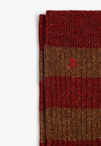 Calcetines de rayas en colores rojo oscuro y marrón, con textura acanalada, y un pequeño logo de calavera roja en el puño. Material suave de punto.