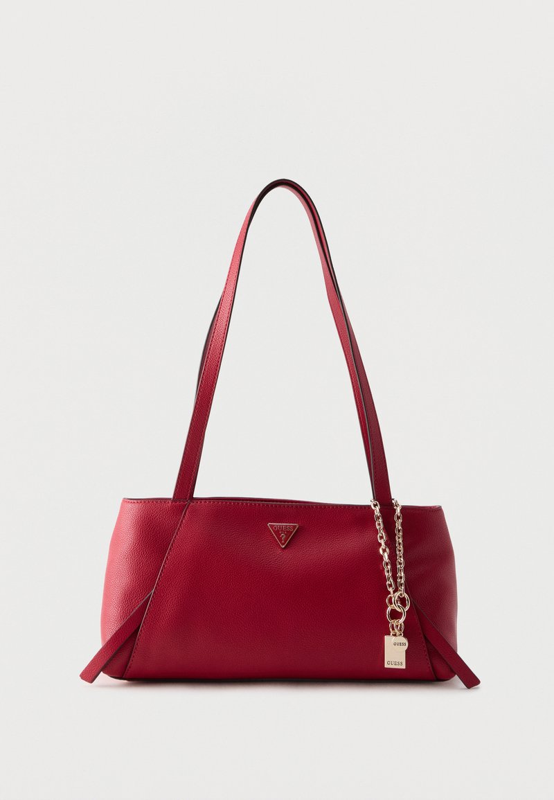 Sac à bandoulière en cuir rouge avec double bandoulière, logo triangulaire Guess et chaîne dorée avec breloque cadenas sur un fond clair uni.