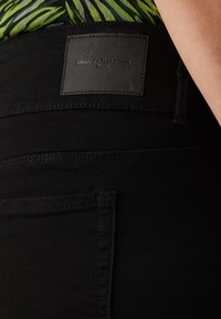 Czarne jeansy z denimu z skórzaną metką marki, płaskie szwy i widoczne kieszenie z tyłu. Gładka faktura i dopasowany krój.