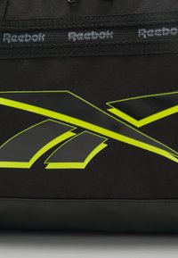 Black sports bag featuring large gray and vibrant yellow Reebok logo accents. Made from durable fabric with reinforced stitching and handles.