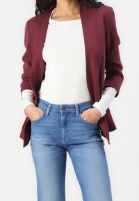 Bordeauxrode blazer met sjaalkraag, gecombineerd met een wit topje met lange mouwen en lichtblauwe spijkerbroek. Gladde textuur, op maat gemaakte pasvorm en zakdetails.