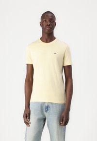Tricou din bumbac galben, cu mâneci scurte și guler rotund, având un mic logo roșu, alb și albastru pe pieptul stâng.