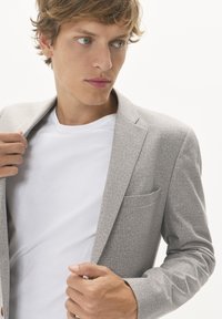 Ljust grå blazer i en texturerad tygkvalitet, med en enkel ficka och notch-krage, parat med en enfärgad vit t-shirt under.