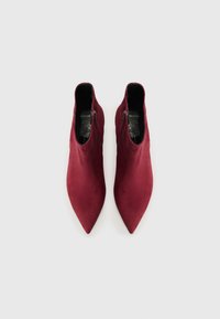 Bottines bordeaux en daim avec un design à bout pointu et fermeture éclair sur le côté, présentant une texture lisse et un style minimaliste.