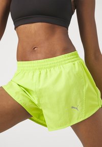 Pantalones cortos deportivos de color verde neón con un panel de malla transpirable, cinturilla elástica y un pequeño detalle en logo plateado en el lado. Material ligero.