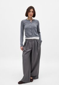 Gray cardigan with a round neck and front buttons, paired with high-waisted, wide-leg gray pants. Soft texture and relaxed fit.