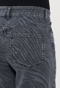 Črne jeans hlače iz denima z diskretnim vzorcem tigrove črte, strukturiran zadnji žep in standardnim šivinami ob šivih.