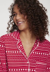 Crvena pidžama s uzorkom, bijelim geometrijskim dizajnom i cvjetnim akcentima, s ovratnikom, kopčanjem na gumbe i džepom na prsima.