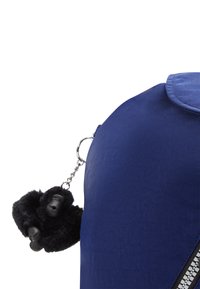 Zaino blu navy realizzato in tessuto textures, con cerniera e un portachiavi gorilla peloso nero attaccato da una catena metallica.