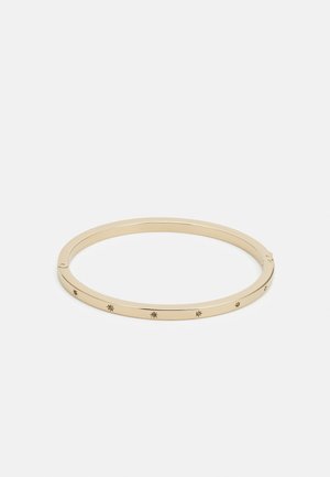 Dunne armband in goudkleur met kleine gegraveerde sterren- en zonvormen gelijkmatig verdeeld rondom, op een witte achtergrond.