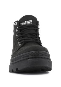 Botín negro de tobillo con material duradero, puntera redonda, suela de goma texturizada y etiqueta de logo blanca en contraste. Presenta ojales de metal y cordones.