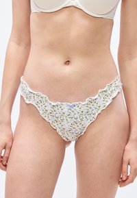 Femme portant un bikini blanc à volants avec de petites fleurs bleues et vertes et un nœud bleu au centre devant.