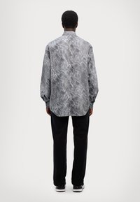 Long-sleeve button-up shirt in gray and black snake print, with a relaxed fit and round hem. Paired with black pants and sneakers.