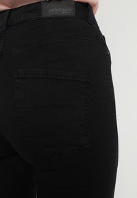 Jeans de mezclilla negra con una textura suave, que cuentan con un bolsillo trasero y una etiqueta que dice "jeans perfectos" en la cinturilla.