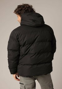 Doudoune noire avec capuche, dotée d'un design matelassé et de poignets élastiques. Le matériau semble épais et isolant pour garder au chaud.