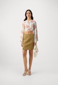 Balta cropped blūze ar korallkrāsas ziedu rakstu, apvienota ar khaki mini svārkiem ar sānu šķēlumiem un baltām papēžkurpēm. Tur rokās baltu somu.