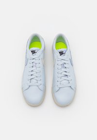 Zapatillas de deporte azul claro con una parte superior de cuero suave, puntera redonda, suela de goma plana y un chorro blanco en contraste; cuentan con una plantilla de un vibrante verde neón.