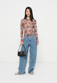 Langermet tettsittende skjorte med et fargerikt grafisk trykk på et gjennomsiktig materiale, kombinert med vide blå jeans og en liten svart håndveske.