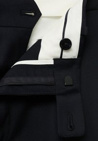 Black suit jacket with white shirt cuff showing a black button and a zippered inner pocket.