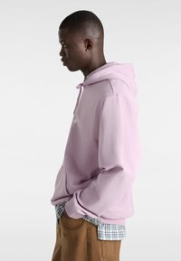 Sudadera con capucha morada con un bolsillo delantero, superpuesta a una camisa de cuadros azul y blanca, combinada con pantalones marrones. Diseño sencillo y textura suave.