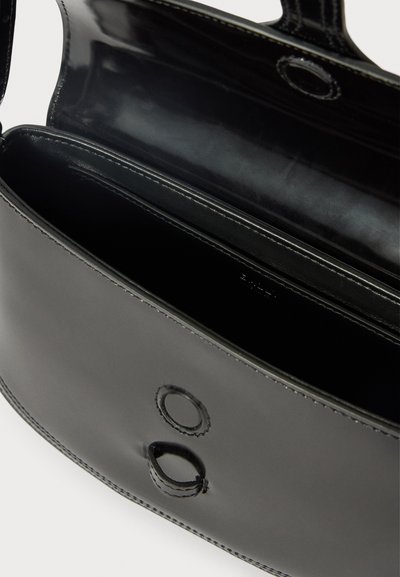 Black leather bag with a sleek design, featuring a smooth texture, two circular accents, and a spacious interior with no visible compartments.