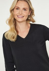 Pulover negru cu decolteu în V, cu mâneci lungi, fabricat dintr-un material moale și texturat. Prezintă un design simplu și o croială lejeră.