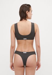 Súprava tmavo sivej bikiny, ktorá obsahuje športový top s okrúhlym výstrihom na chrbte a zodpovedajúce dno v thong štýle. Textúrovaná látka s minimálnym brandingom.