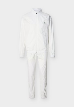 Hvitt treningssett med jakke med hel glidelås og matchende bukser, begge med elastiske mansjetter og en liten grønn krokodillelogo på venstre bryst.