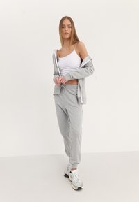 Set di pantaloni tuta grigi e felpa in morbido tessuto, con vestibilità rilassata, vita con coulisse e tasche a marsupio, abbinato a una canotta bianca.