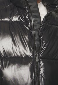 Schwarze Pufferjacke aus glänzendem Nylon, mit hohem Kragen, durchgehendem Reißverschluss und dezentem Logo-Detail am Reißverschluss.