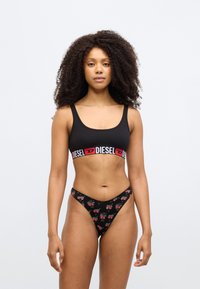 Mustast puuvillast spordirinnahoidja punase ja valge "DIESEL" logoga paelaga. Must tangatüüpi aluspüksid punaste südamemustritega ja V-kujulise vöökohaga.