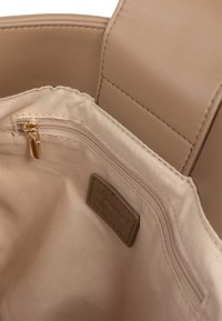 Indvendigt i beige håndtaske med en glat, tekstureret finish, der har en lynlåslomme og et lille logo-tag i en lysere nuance.