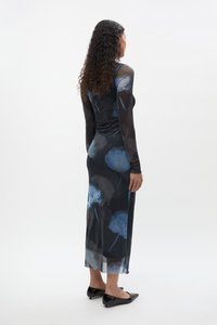 Garš melns kleita ar zilu ziedu rakstu, caurspīdīgas garas piedurknes, pieguloša augšdaļa un taisns griezums. Ar kleitas apakšmalu zem ceļa un melnām plakanām kurpēm.