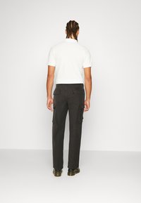 Witte polo met korte mouwen, gecombineerd met donkere cargo broek met zijzakken, een gladde textuur en een recht model.