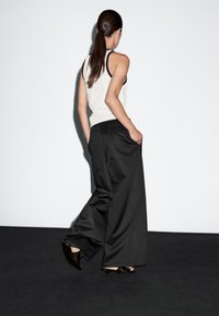 White tank top and black wide-leg trousers, with a smooth texture. The trousers feature pockets and a relaxed fit. Black shoes with low heels.