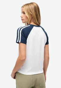 Kortærmet raglan t-shirt i marineblå og hvid, med hvide striber på skuldrene og en afslappet pasform. Fremstillet af bomuld.
