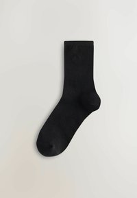 Svarta ribbade strumpor med förstärkt tå och häl, med en liten, diskret logotyp nära vristen. Tillverkade av ett mjukt, stretchy material.