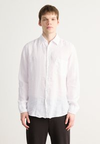 Camisa de lino blanca de manga larga con collar abotonado, un bolsillo en el pecho y un corte relajado; tejido texturizado con un aspecto ligeramente arrugado.