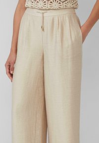 Brede beige broek gemaakt van lichtgewicht stof. Voorzien van een trekkoord in de taille en zijzakken. Soepele textuur met een subtiele glans.