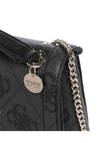 Borsa nera in tessuto con catena e manico in pelle, con design embossato e un'etichetta metallica con la scritta "GUESS EST.1981".
