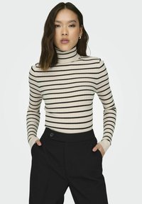 Striped turtleneck sweater in cream with black horizontal stripes, fitted design, ribbed texture, paired with high-waisted black trousers.