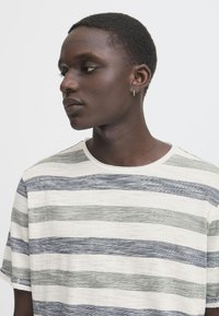 Randig t-shirt med rund halsringning, tillverkad av lätt tyg, med horisontella linjer i marinblått, grönt och krämfärgat. Korta ärmar, avslappnad passform.