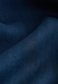 Tissu en lin bleu marine avec une texture lisse, présentant des variations subtiles dans le tissage et la réflexion de la lumière, plié en vagues douces.