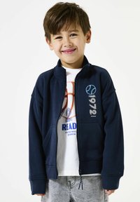 Marine blauwe ritsjack met een hoge kraag, voorzakken en geribde manchetten. Bevat geprinte graphics in wit en turquoise. Soepele stofstructuur.