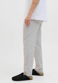 Pantalons gris clair, amples, en tissu doux, avec une coupe droite, associés à des chaussures noires à enfiler et une chemise blanche.